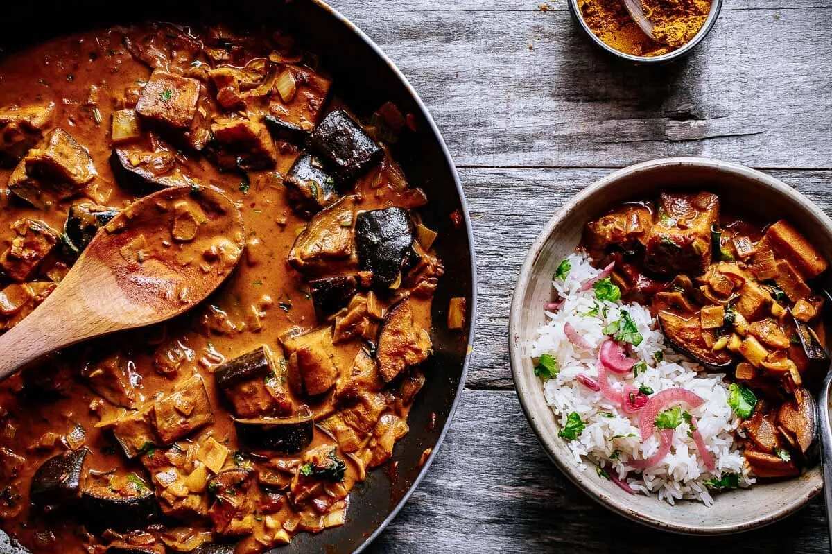 Thumbnail image of roasted aubergine curry with tomato sauce and rice, garnished with fresh coriander, served on a beige ceramic plate. How to Cook Aubergine