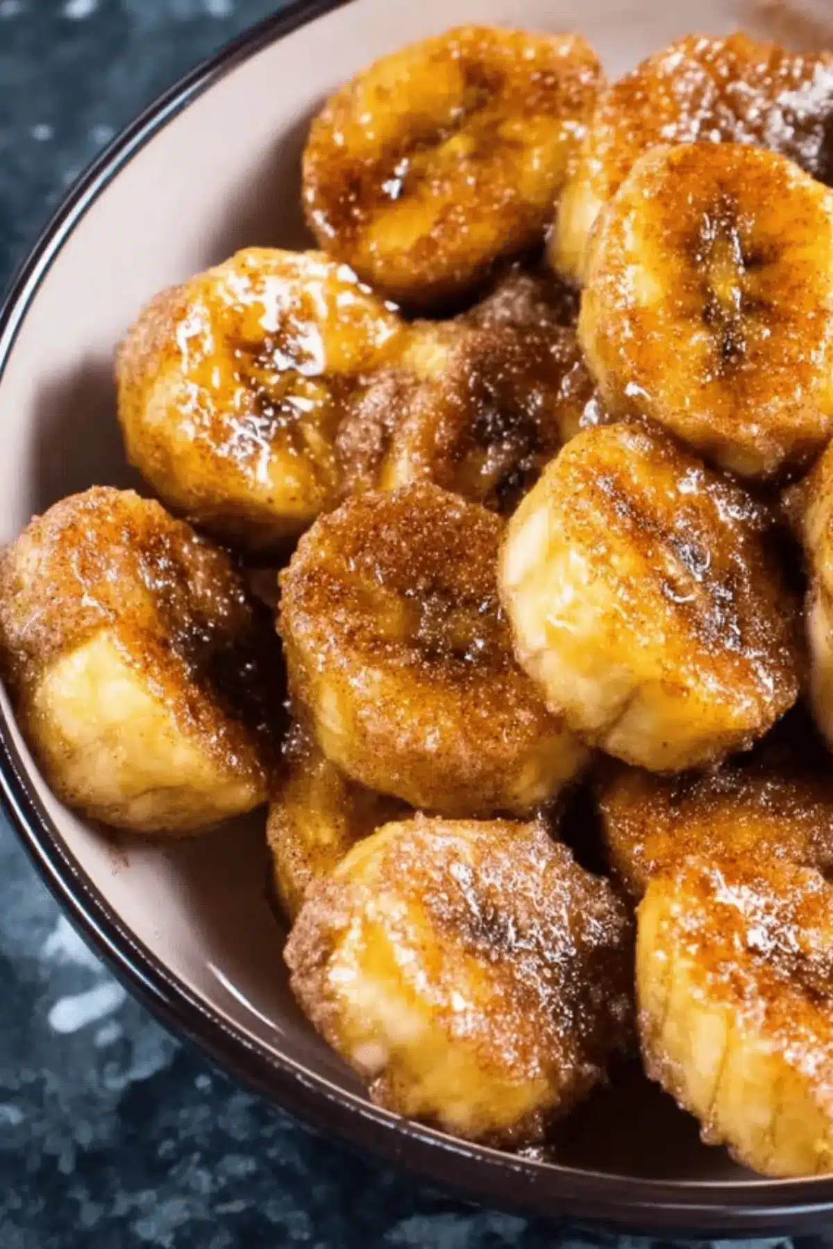 Close-up of golden air fried banana slices coated with cinnamon and brown sugar, served in a bowl – a quick and healthy sweet snack.