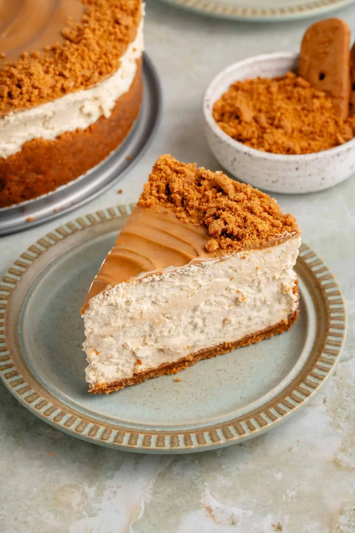 Close-up of a creamy no-bake Biscoff cheesecake slice topped with cookie butter and crushed Biscoff biscuits on a ceramic plate