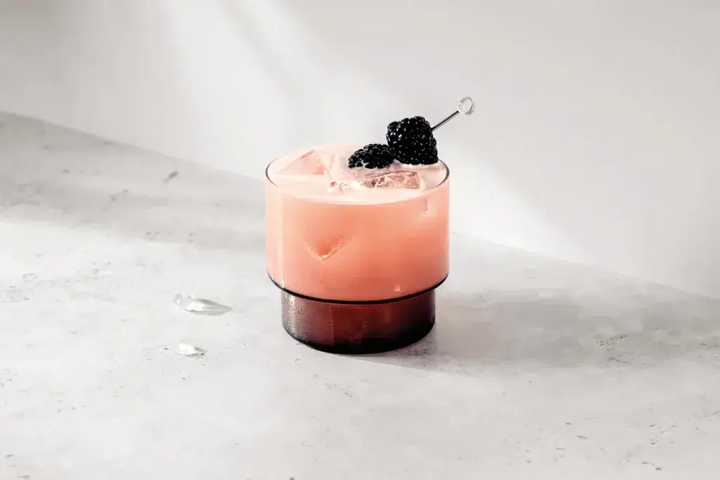 Bramble Cocktail served over ice in a short glass, garnished with fresh blackberries on a cocktail pick – classic gin drink with a fruity twist