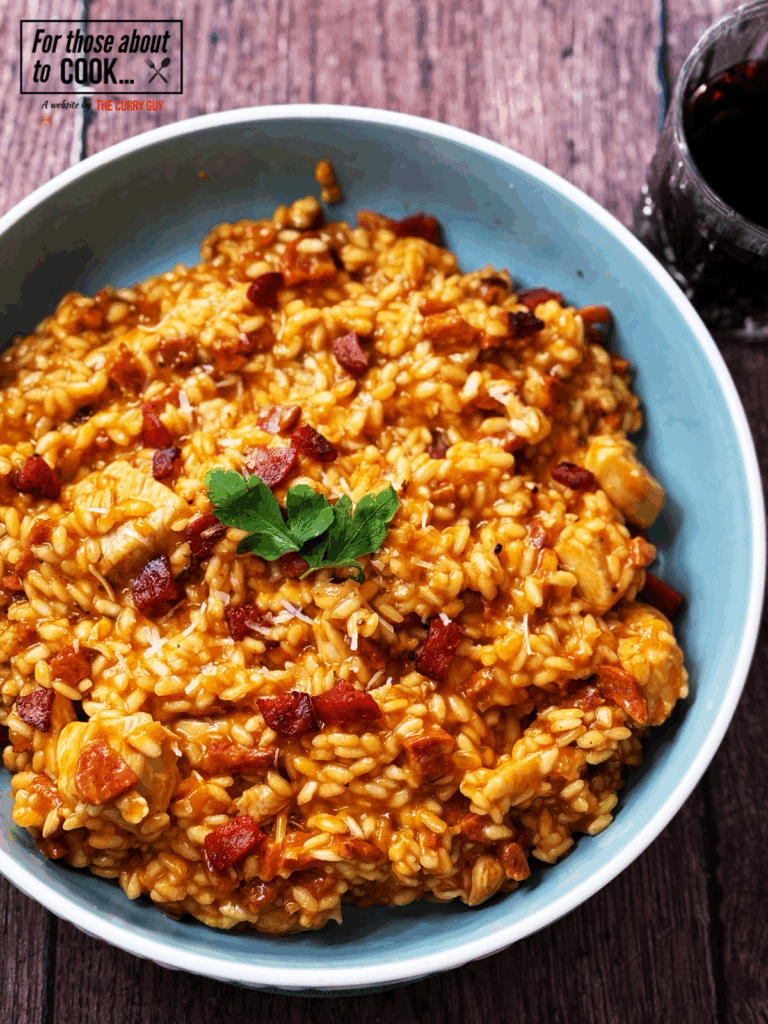 Creamy chicken and chorizo risotto served in a blue bowl, topped with parsley and crispy chorizo pieces, perfect comforting dinner recipe.