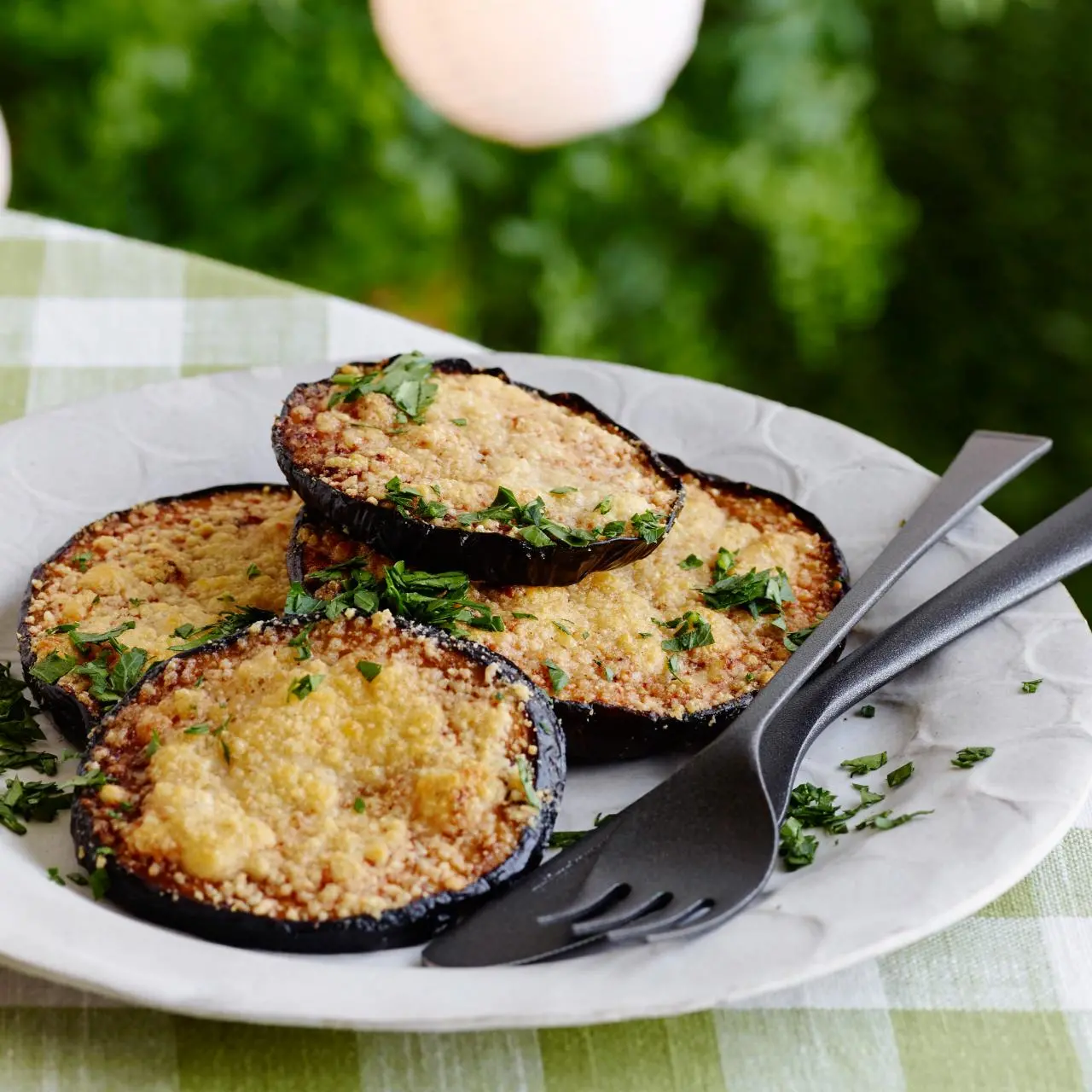 Grilled eggplant steaks with charred golden-brown grill marks, garnished with fresh parsley on a dark serving platter. How to Cook Aubergine