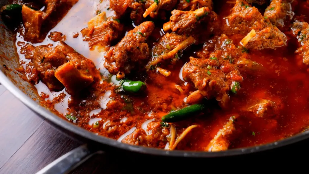 Close-up of a rich and aromatic lamb karahi, featuring tender chunks of lamb simmered in a spiced tomato-based gravy with fresh green chilies and ginger strips, served in a deep cooking pan. One-Pot Lamb Karahi